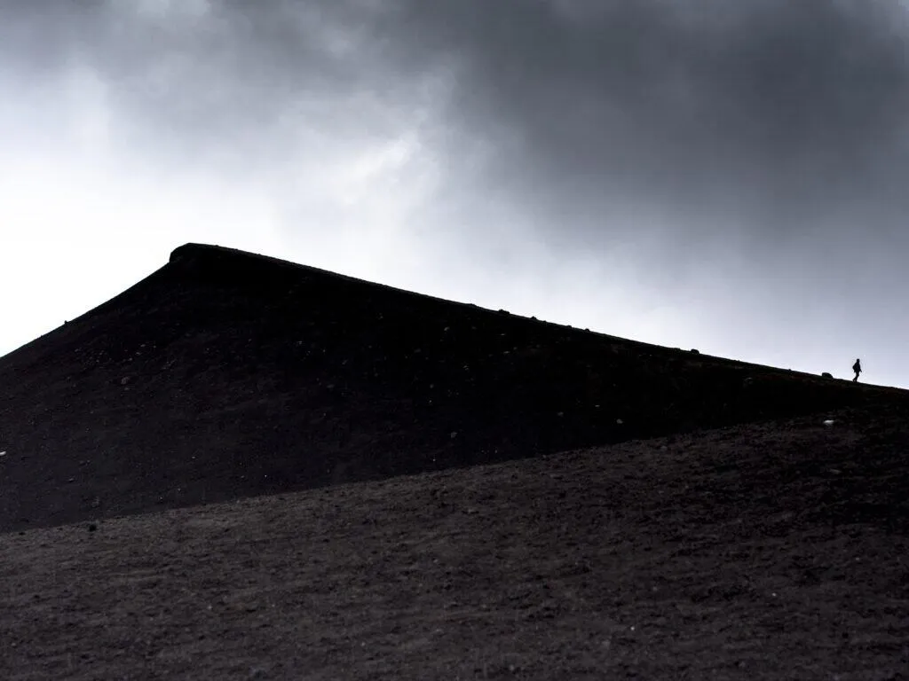 pair A lone figure on the black cinder slope of Etna under heavy cloud