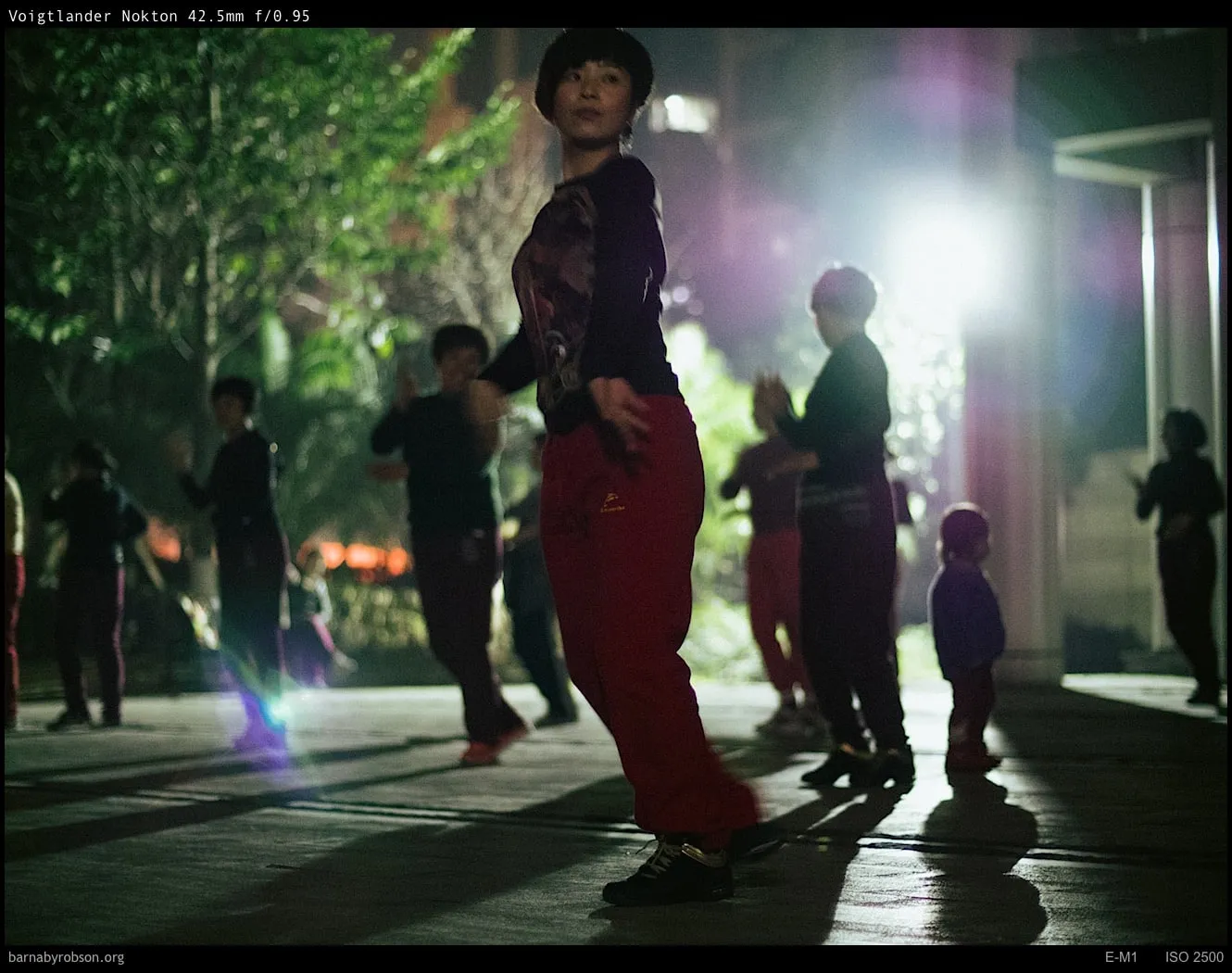Woman in red trousers and others dancing outdoors at night.