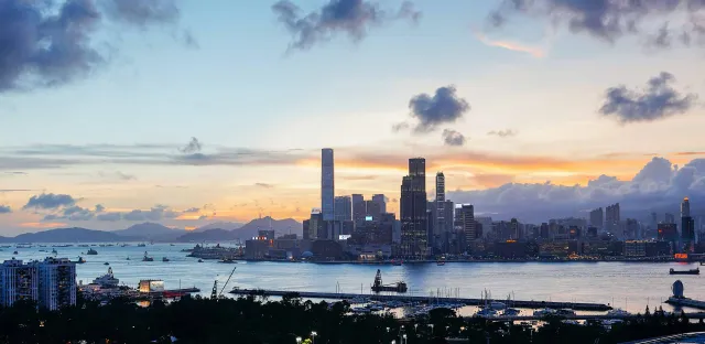 Victoria Harbour at dusk under an amber sky, the ICC and Kowloon skyline lit against the water