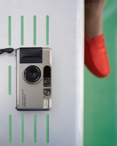 Contax T2 resting on a green-slotted bench beside a red loafer