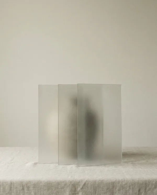 A minimal still-life photograph of three tall frosted translucent panels standing and gently overlapping on a pale surface in soft light — knowledge, power and money.