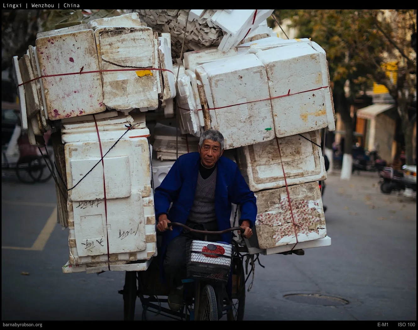 Man on bicycle heavily loaded with dirty white polystyrene boxes.